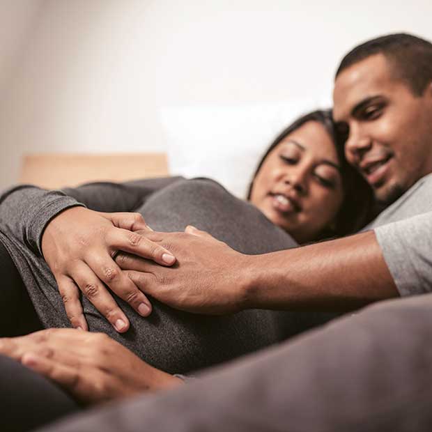 Pregnant couple place hands on belly