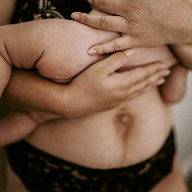 Postpartum mother holds her newborn baby skin-to-skin on her belly