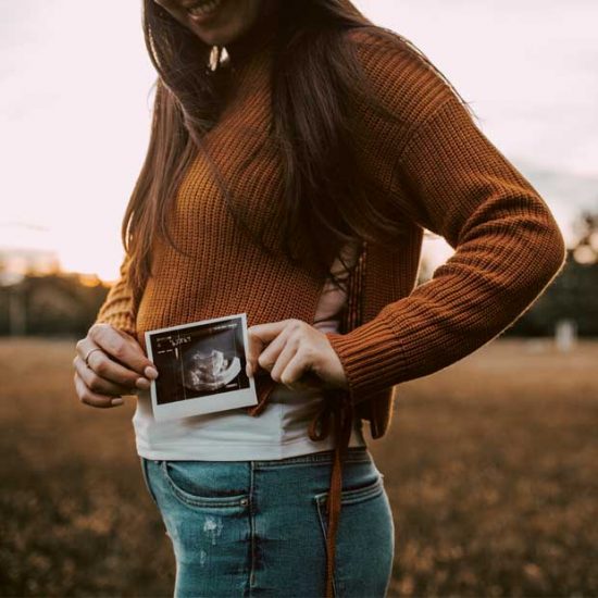 Woman holds up ultrasound scan photo next to belly