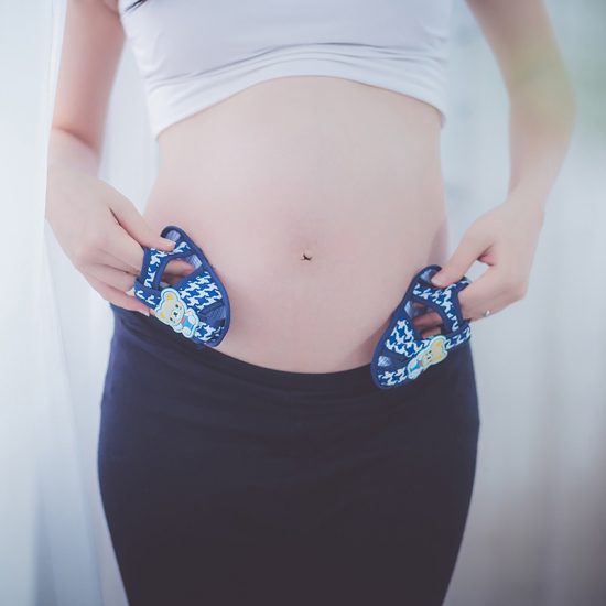 Mum holds baby shoes up to pregnant belly
