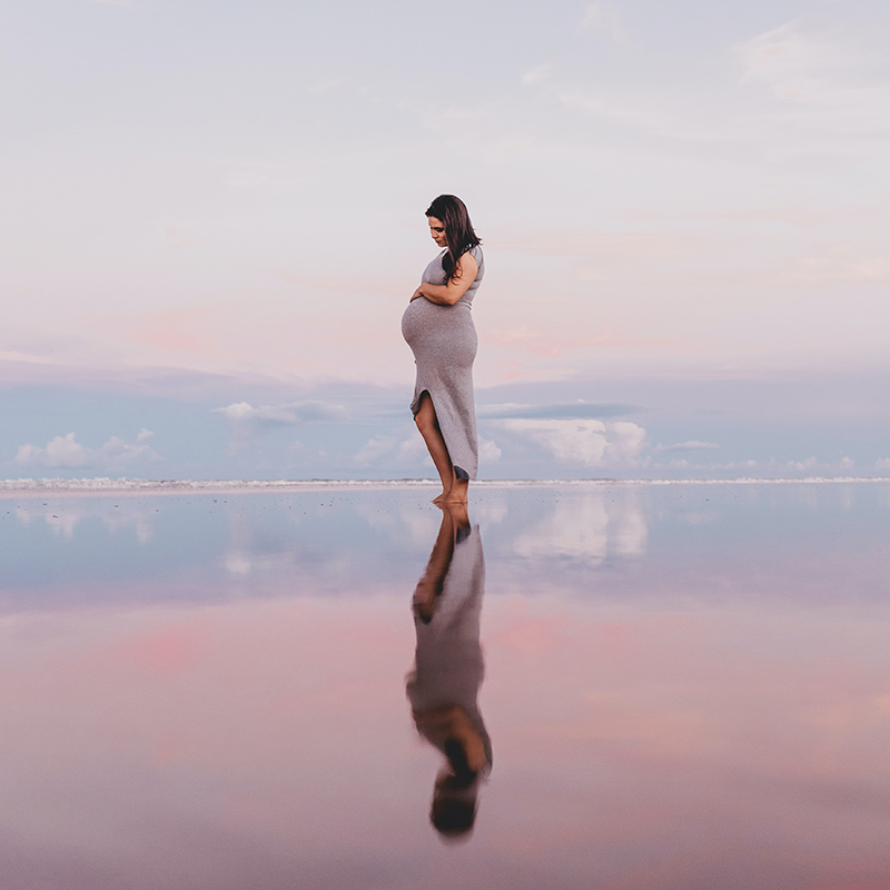 Pregnant woman at sunset holds her belly